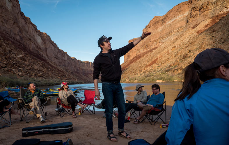 A man points at the canyon walls in front of a seated group