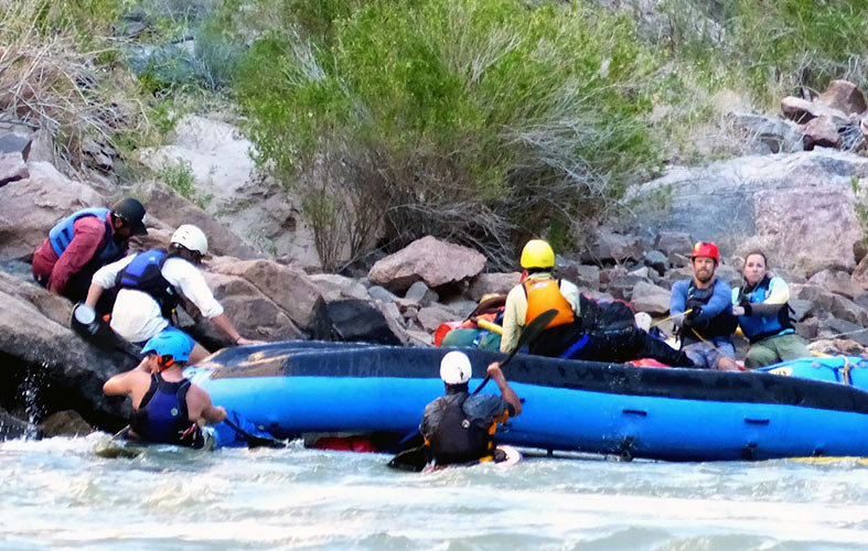 Members of the team help rescue a crew of a flipped boat on the shores of the Colorado River
