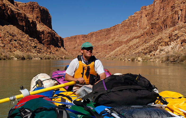 A river guide paddling a boat full of gear down the Colorado River