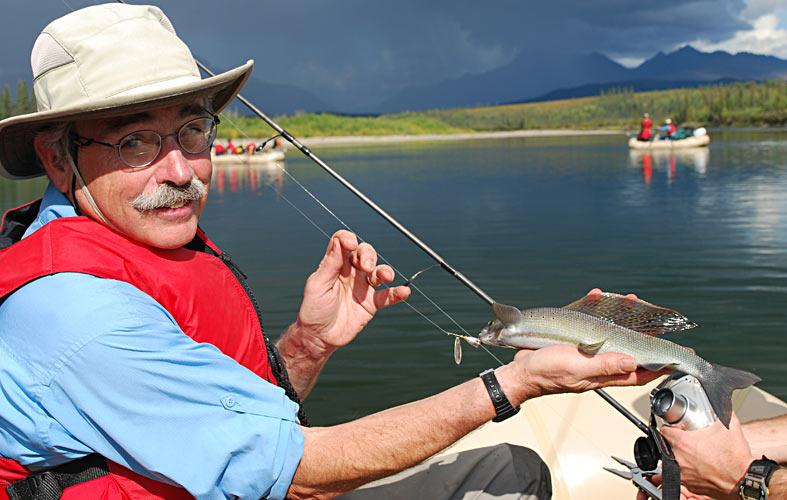 Peter Moyle holds a fish fish in his hand that he caught from his raft on a river in Alaska